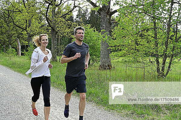 Couple running on dirt road against trees in forest
