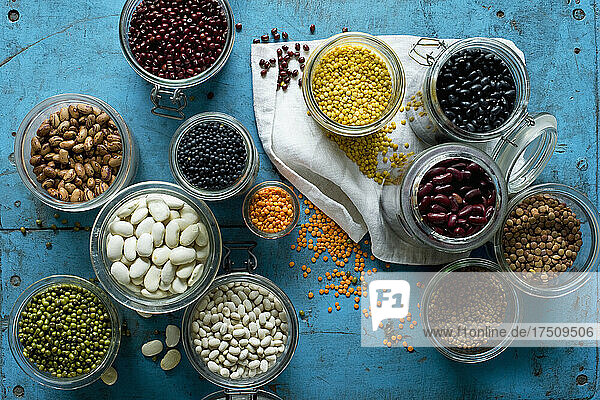 Various beans and lentils in jars on blue rustic wooden surface