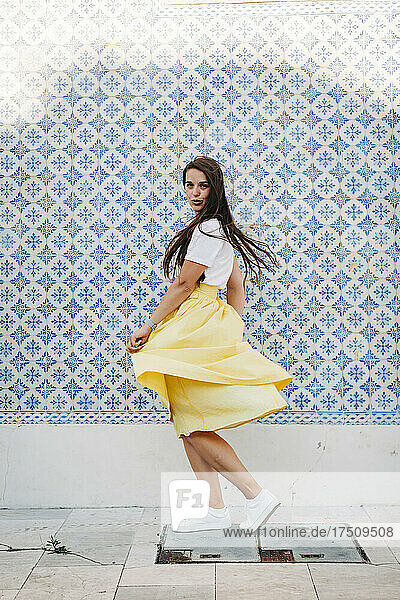 Beautiful woman with long hair spinning on street against tiled wall in city