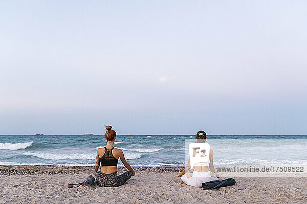 Young women meditating on beach against clear sky during sunset