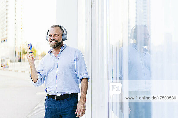 Businessman holding smart phone while listening music in city
