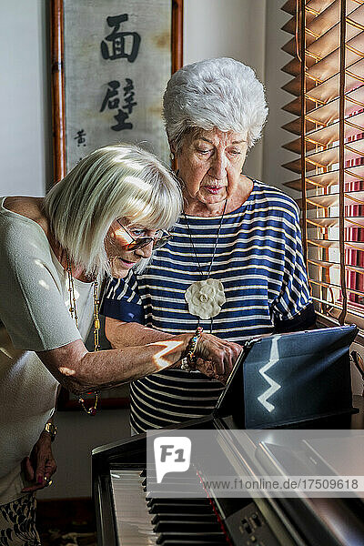 Senior female friends using digital tablet on piano at home