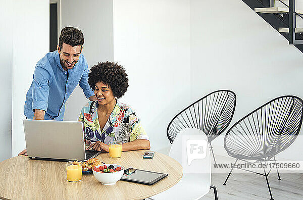 Happy couple using laptop at dining table in modern penthouse