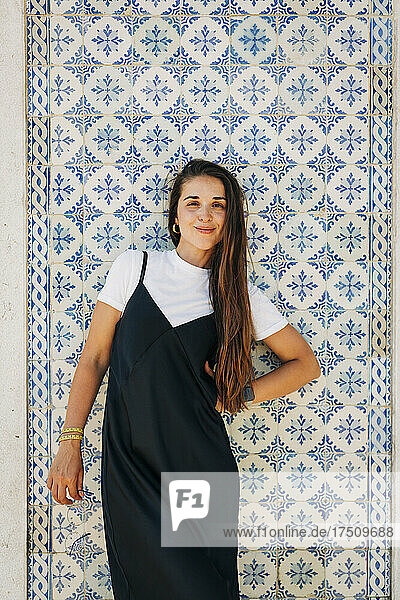 Smiling beautiful woman with long hair standing against tiled wall in city