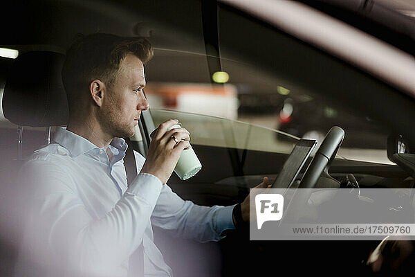 Businessman with coffee reading online on digital tablet in car
