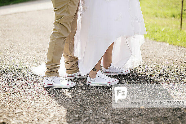 Unterer Teil eines Paares in weißen Schuhen mit dem Text „König und Königin“  das auf einer unbefestigten Straße steht