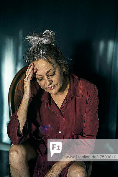 Sad senior woman with head in hand sitting on chair at home