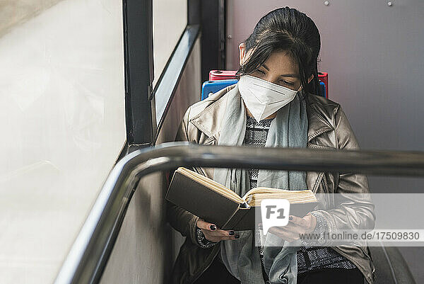 Woman wearing protective mask while reading book in bus