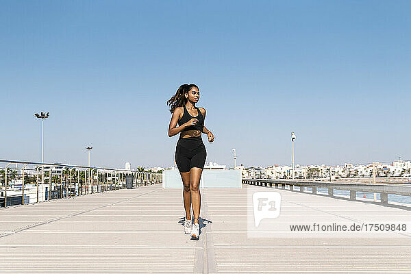 Woman jogging at harbor against clear sky during sunny day