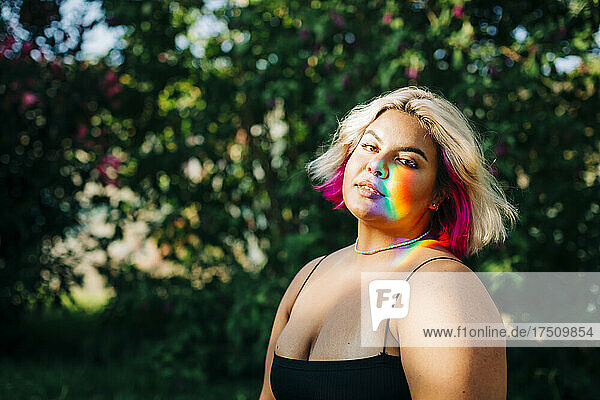 Plus size woman with rainbow lights falling on her face in park