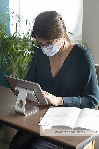 Young woman wearing protective mask using tablet on desk at home