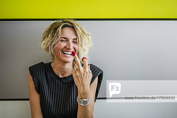 Happy female chef with raspberries on her fingers against wall
