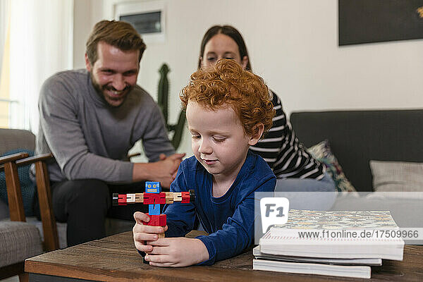 Parents looking at cute son playing with toy robot on table in living room