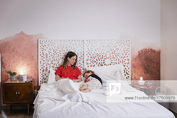 Lächelnde Mutter blickt ihren Sohn an  während sie sich mit ihm im Bett entspannt