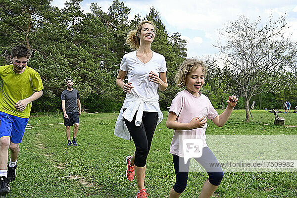 Happy family running on grassy land against trees in forest