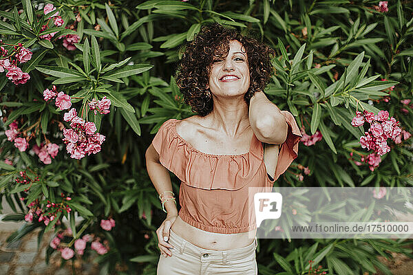 Close-up of smiling mid adult woman with curly hair standing against plants in park