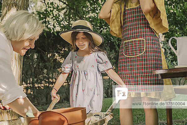 Girl holding wheelbarrow while standing with mother and grandmother in yard