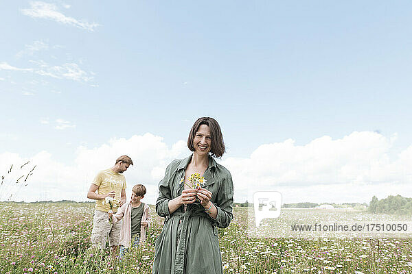 Smiling woman with man and son picking chamomiles in field against sky