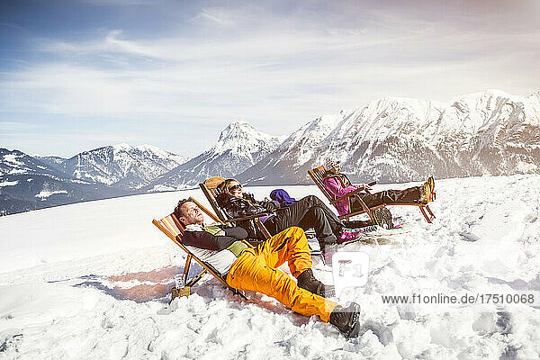 Friends sunbathing in deck chairs in mountainscape in winter  Achenkirch  Austria