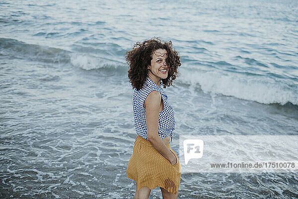Cheerful mid adult woman with curly hair standing in sea during sunset