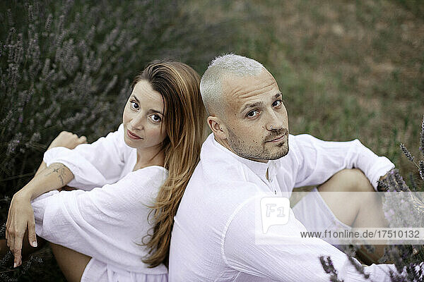 Couple sitting on lavender field looking at camera