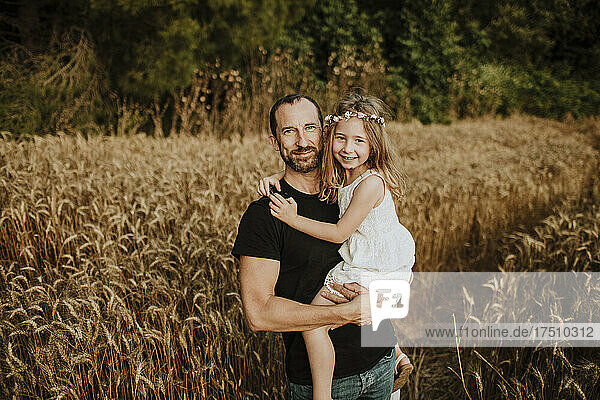 Smiling father carrying daughter in field of wheat