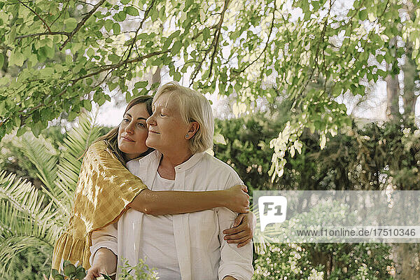 Loving daughter embracing mother while standing against plants in yard