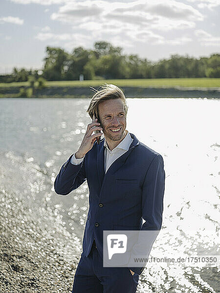Smiling male entrepreneur talking over mobile phone while standing at riverbank