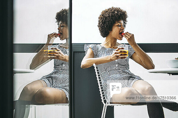 Woman eating strawberry while sitting on chair at balcony in penthouse