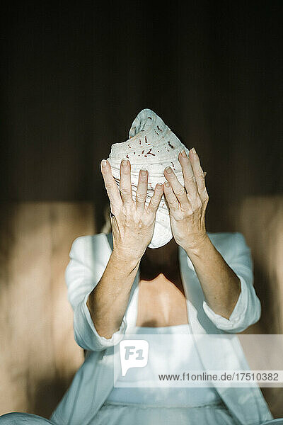 Senior woman covering her face with seashell