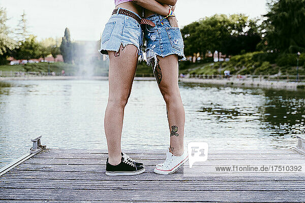 Lesbian couple wearing shorts standing on pier against lake