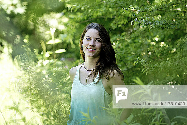Smiling young woman standing amidst plants in forest
