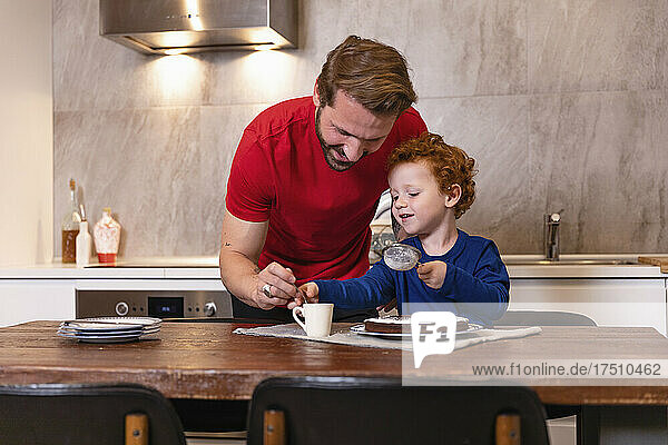 Glücklicher Vater und Sohn dekorieren Schokoladenkuchen auf dem Esstisch in der Küche