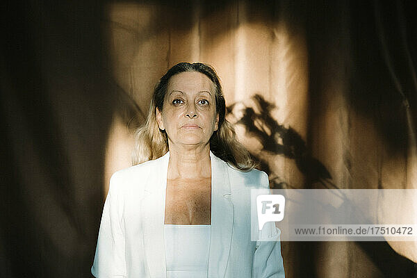 Senior woman standing against curtain in dark