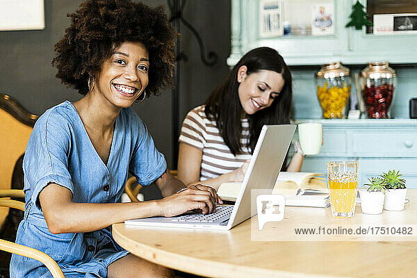 Happy female friends studying with laptop in coffee shop