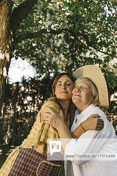 Mutter und Tochter umarmen sich mit geschlossenen Augen im Garten