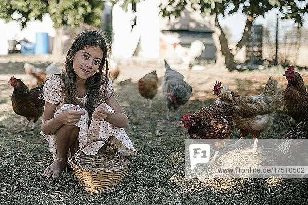Girl with basket sitting in chicken farm