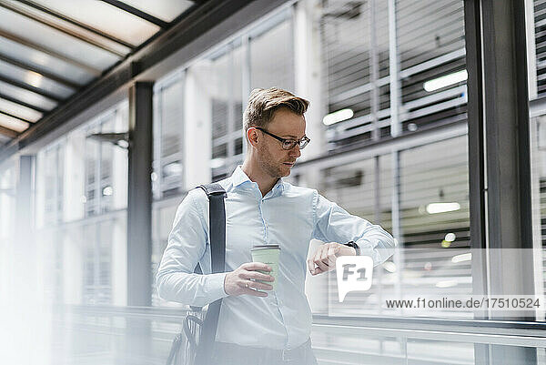 Businessman with coffee checking the time in city