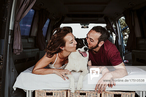 Smiling couple kissing dog while lying in camper trailer