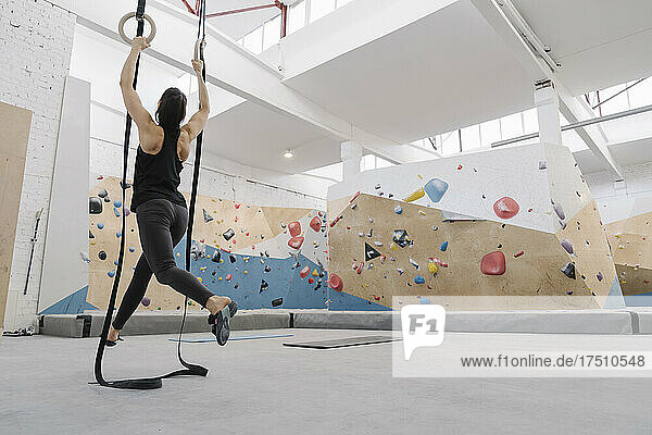 Woman doing stretching exercises on gymanstic rings before climbing on the rock wall