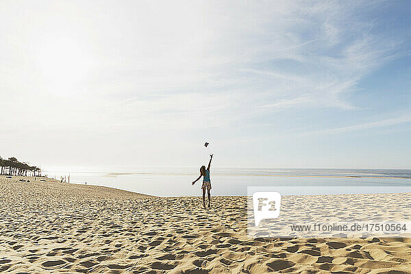 Happy woman throwing hat in mid air while standing at beach against sky  Dune of Pilat  Nouvelle-Aquitaine  France