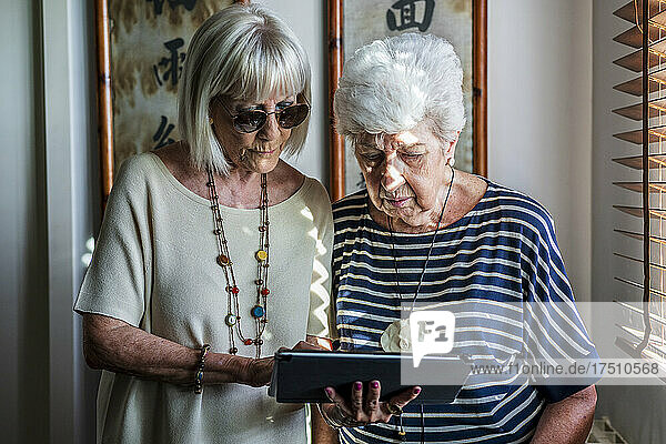 Ältere Freundinnen nutzen digitales Tablet  während sie zu Hause stehen