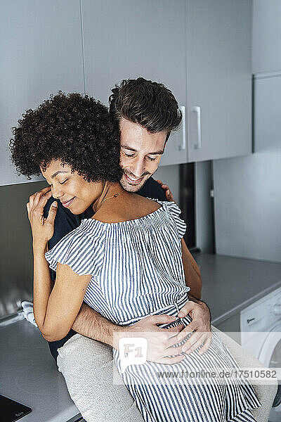 Romantic multi-ethnic couple embracing in kitchen of penthouse