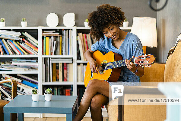 Happy woman playing guitar while sitting on sofa in coffee shop