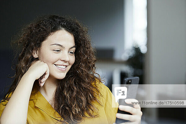 Smiling beautiful woman using smart phone while sitting at home
