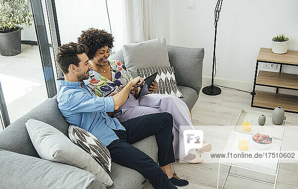 Happy couple using digital tablet while sitting on sofa in penthouse