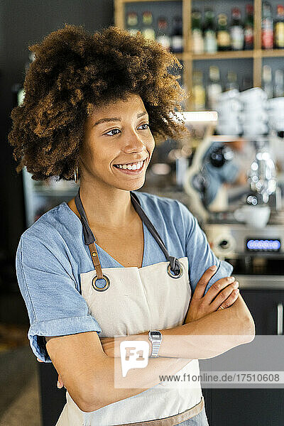 Thoughtful female barista standing arms crossed in cafe