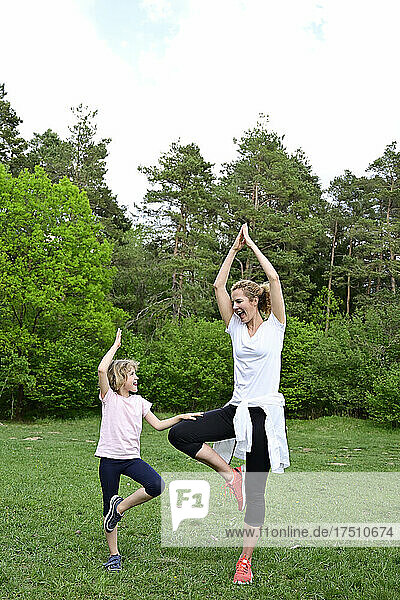 Happy mother and daughter practicing tree pose on grassy land in forest