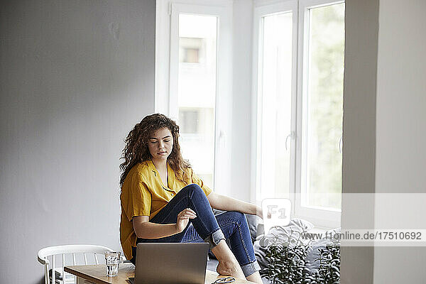 Junge Frau sitzt am Tisch und benutzt Laptop für Online-Hausaufgaben zu Hause