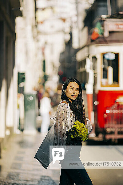 Young woman with bouquet walking in city